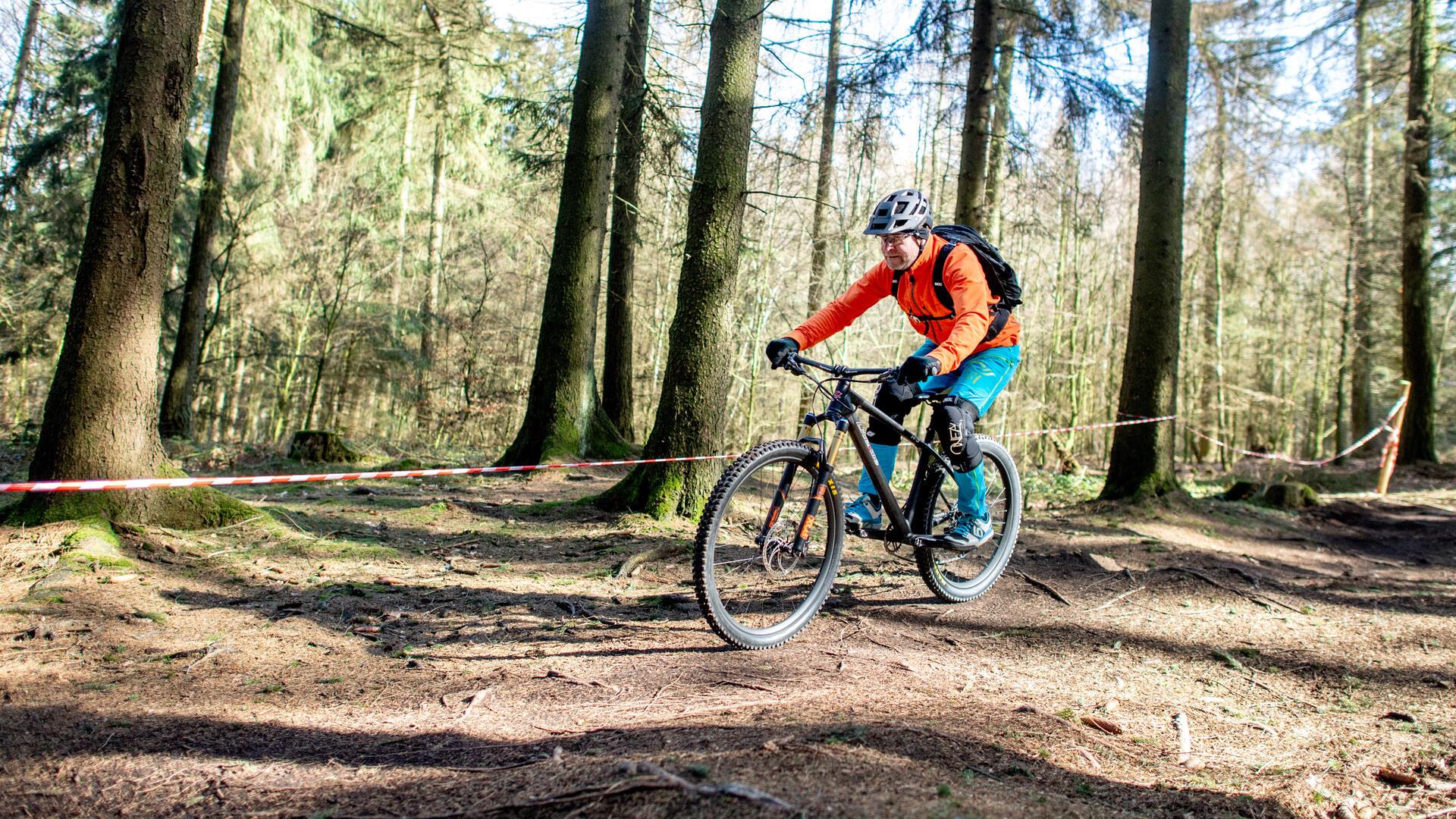 Lars fährt mit seinem Mountainbike auf einer Downhillstrecke durch den Wald im Deister. Bei der Radsportart Downhill geht es um die möglichst schnelle Abfahrt auf einer einer bergab führenden Strecke.
