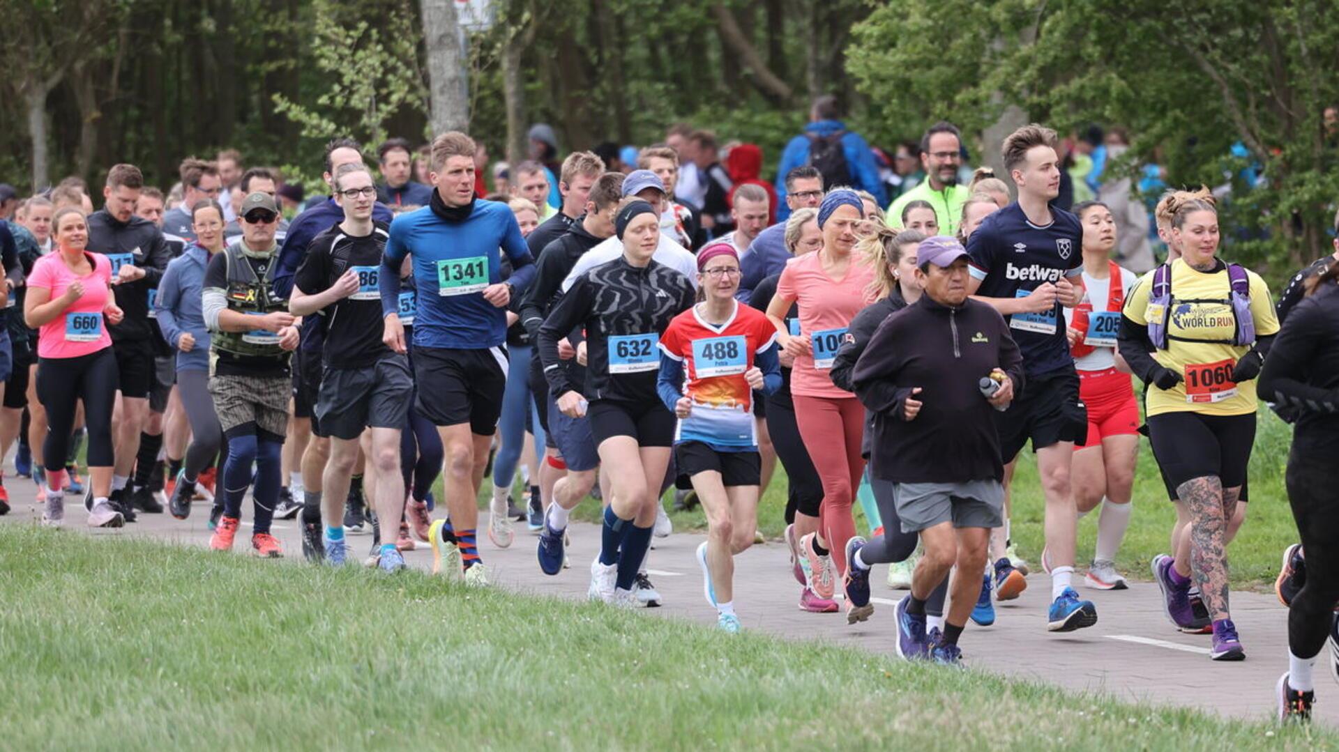 Menschen joggen nebeneinander her. Mehrere Tausend Teilnehmerinnen und Teilnehmer des Cuxhaven-Marathons trotzen den stürmischen Bedingungen auf der neuen Strecke am Deich.