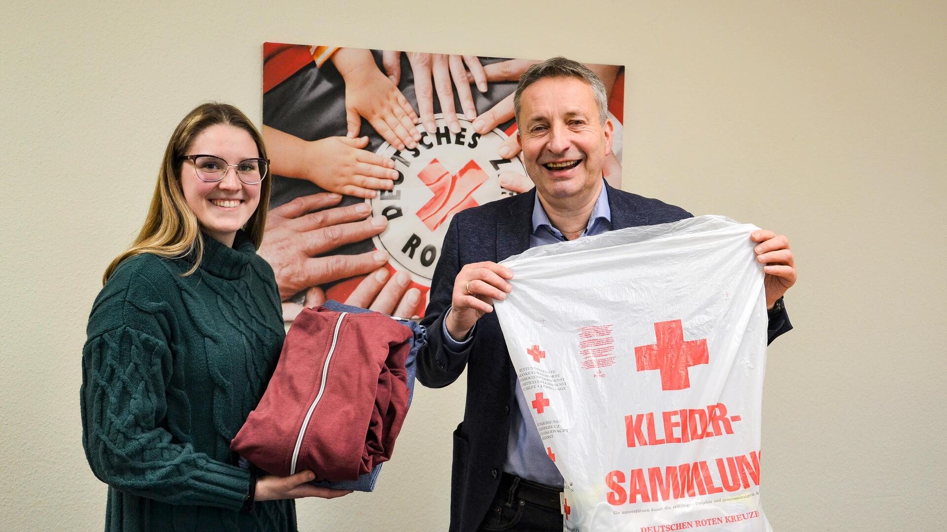 Eine junge Frau und ein Mann halten einen Kleidersack und lächeln in die Kamera.
