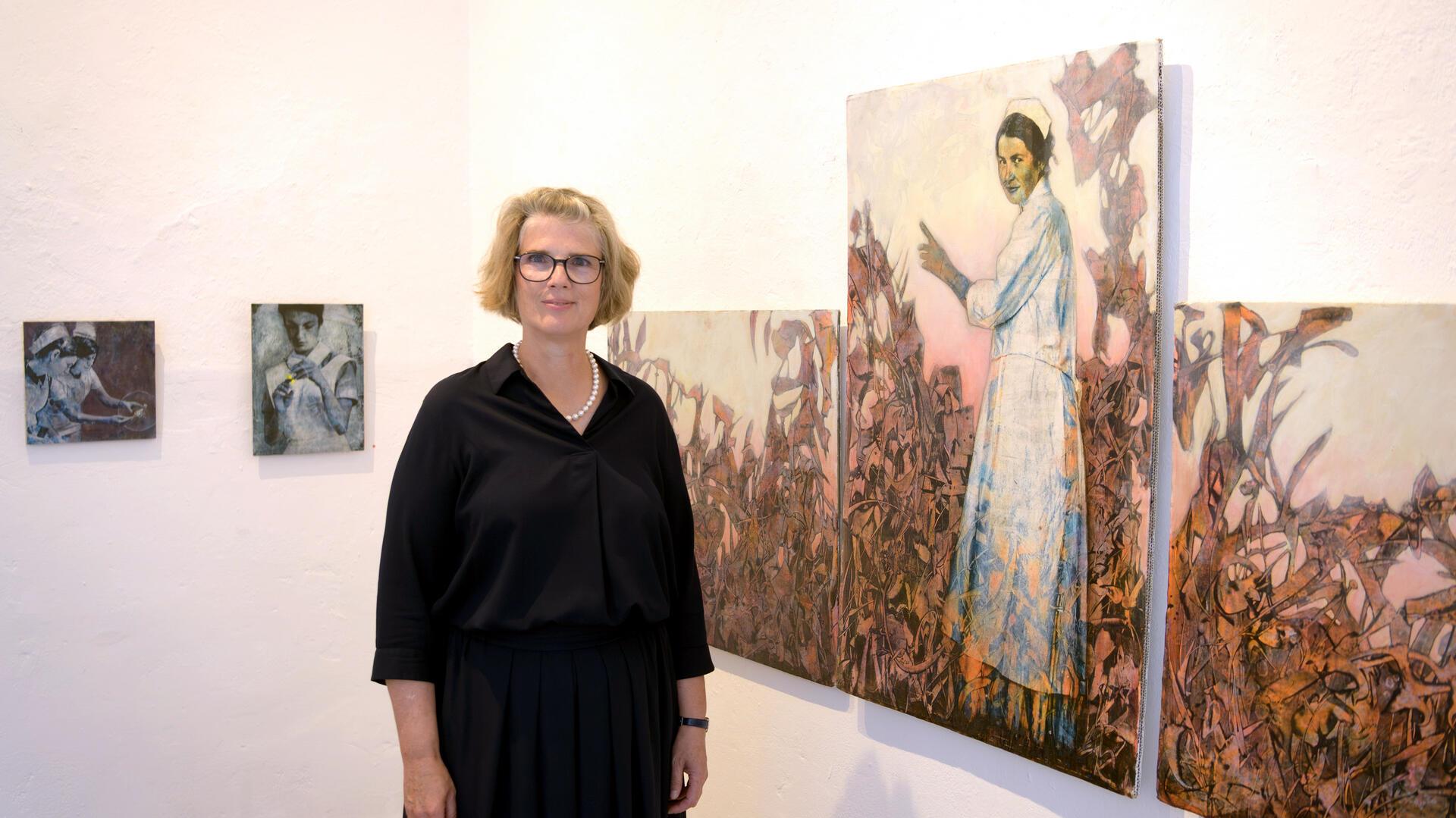 Eine Frau steht vor einem dreiteiligen Bild in einer Galerie. 