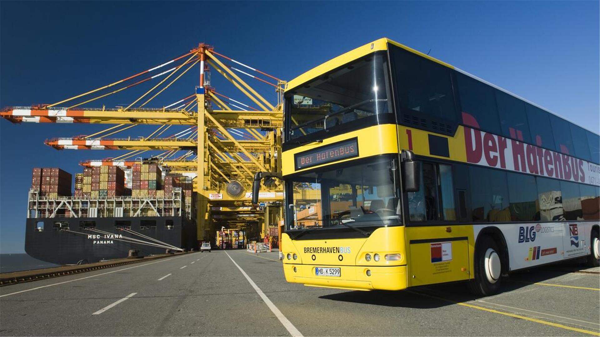 Was kann man in Bremerhaven machen? Tipps für den Besuch in der Stadt am Meer Ein gelber Doppeldecker Bus steht vor einem Containerschiff im Hafen. Die Sonne scheint.