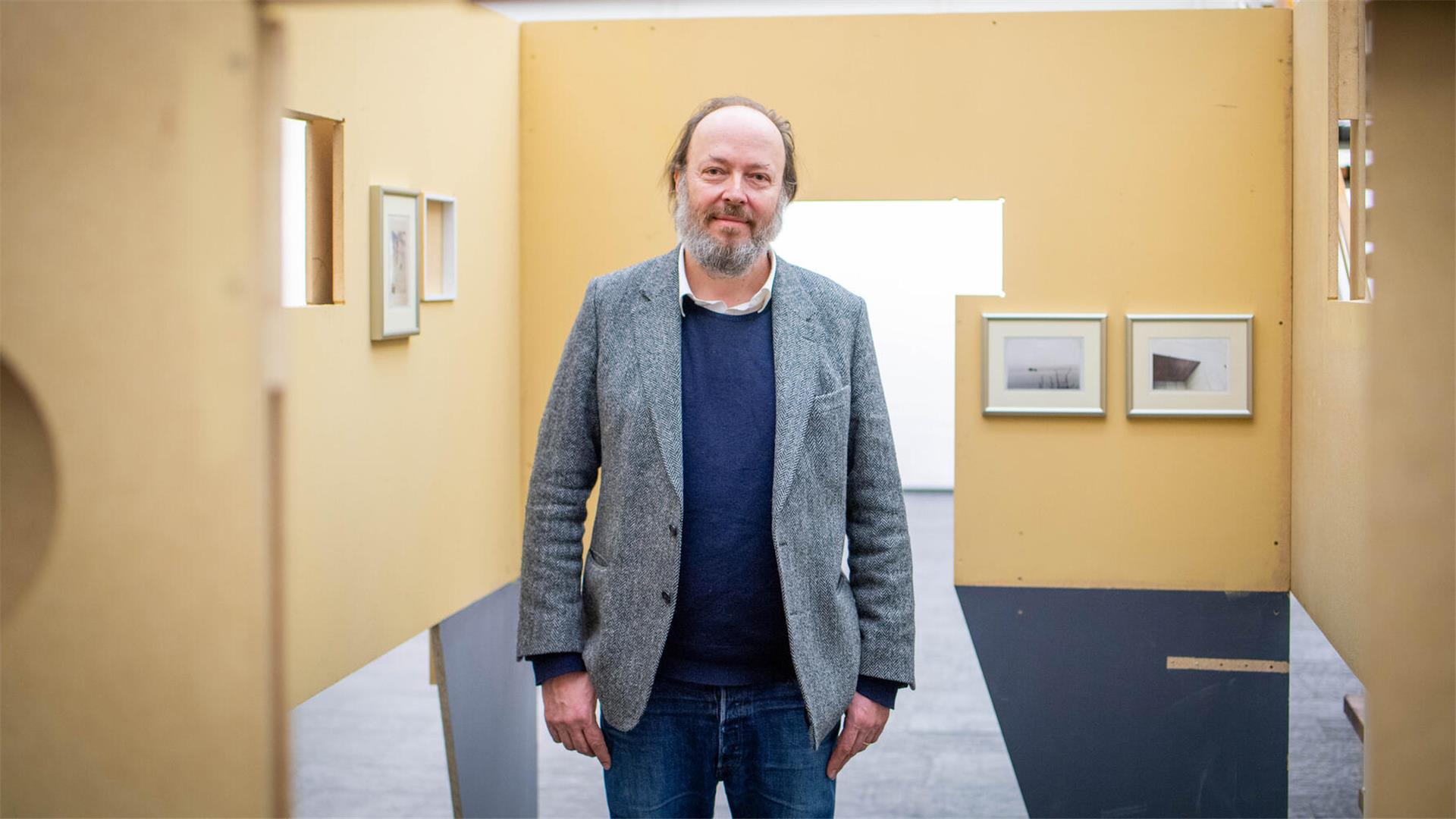 Ein Mann blickt in die Kamera, er steht in einer Ausstellung.