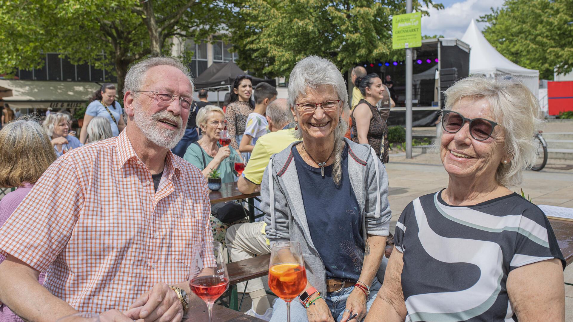 Drei Personen mit einem Glas Wein sitzen am Tisch.