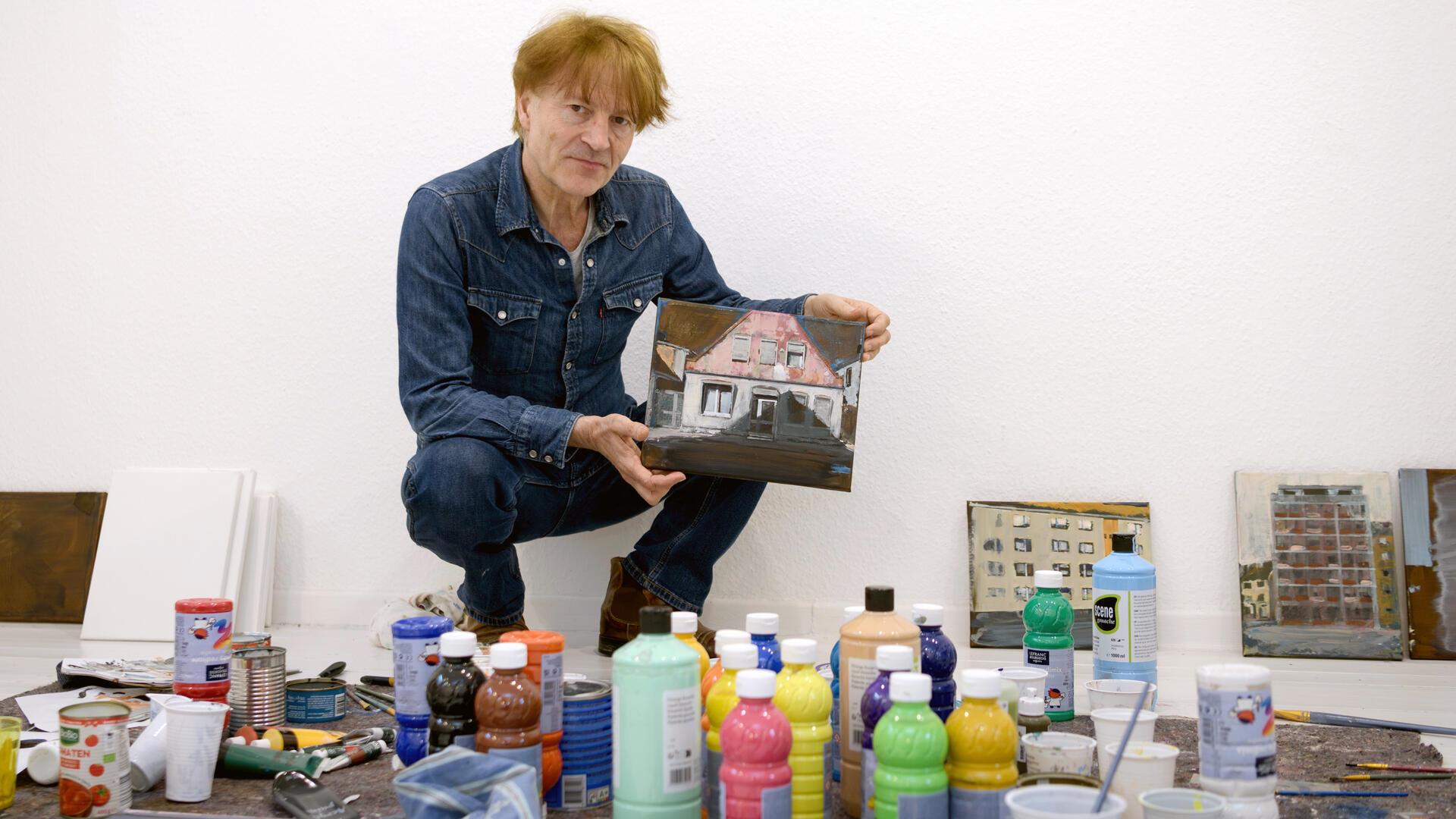 Ein Maler im Atelier. Vor ihm Flaschen mit Farbe.