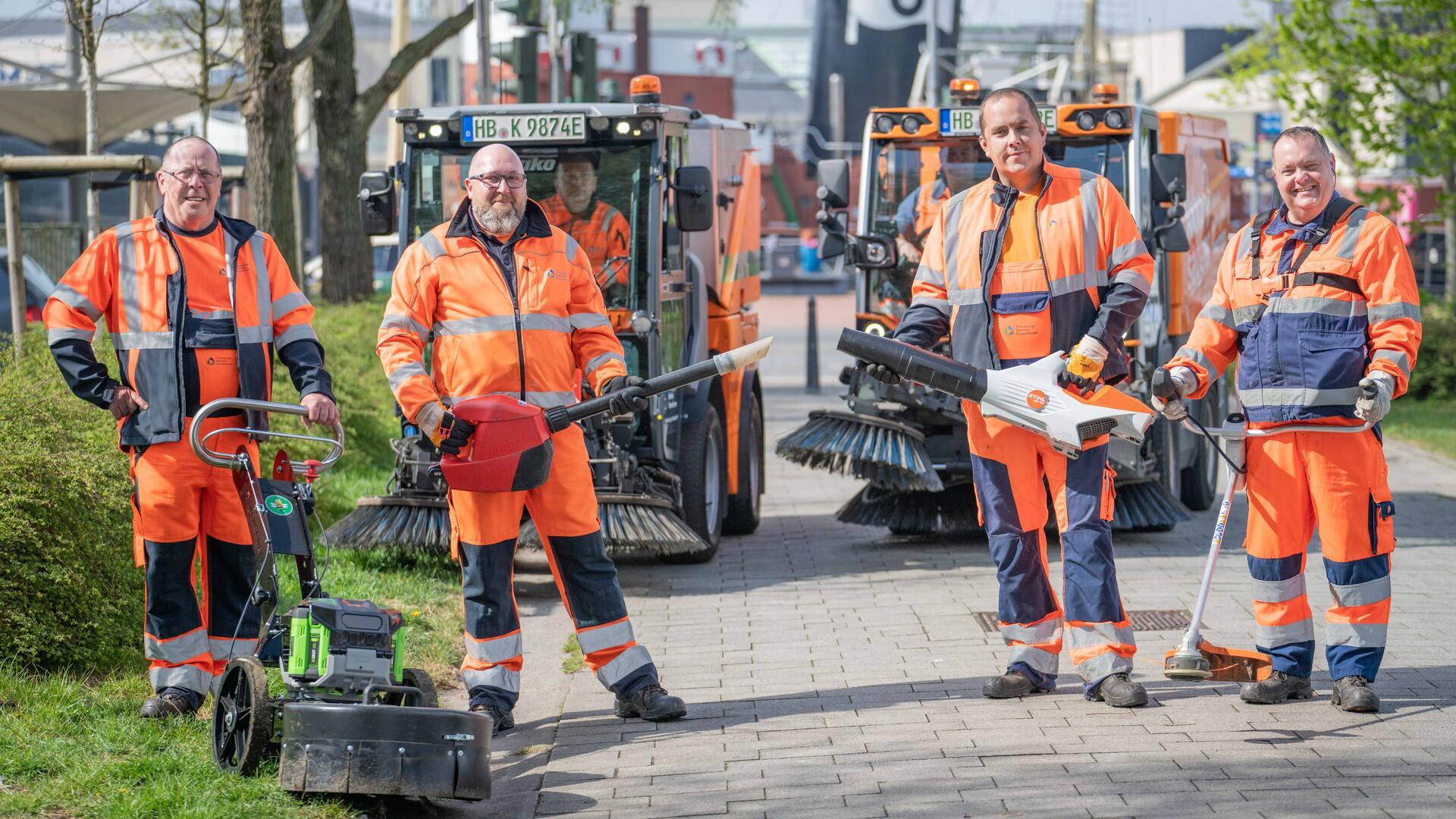 Vier Männer mit Geräten in der Hand stehen auf einem Gehweg