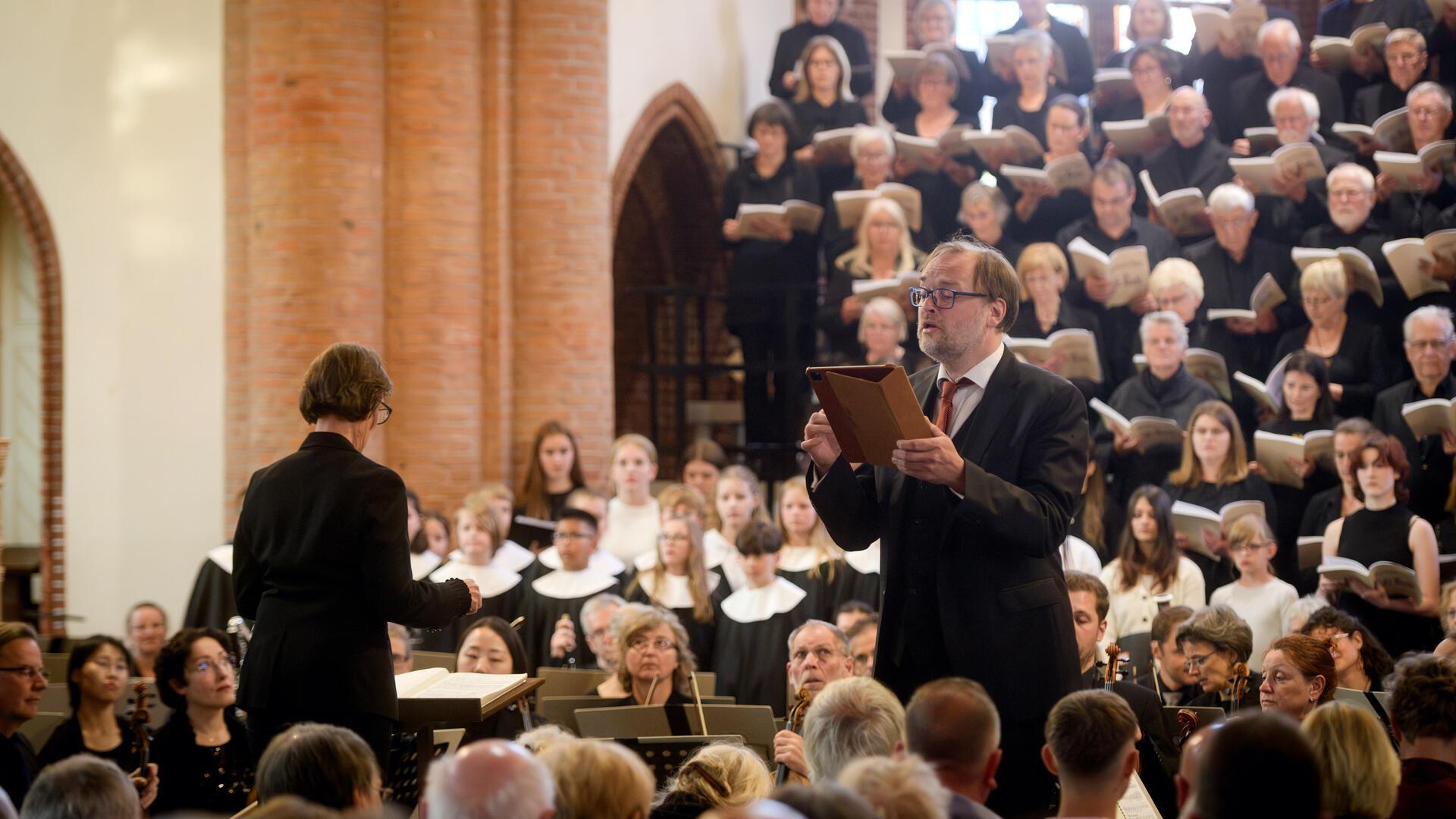 Dirigentin Eva Schad leitet Chor, Orchester und Solisten bei einer Aufführung in der Christuskirche, im Vordergrund ein Solist mit Notenmappe.