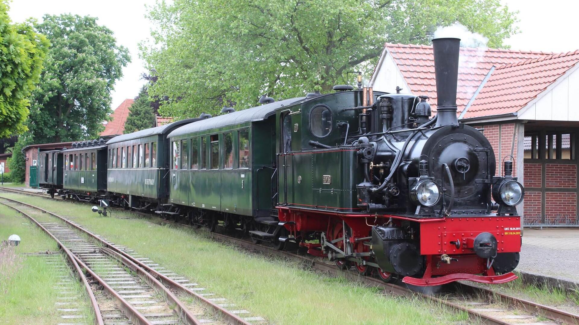 Eine Dampflok steht vor einem Bahnhof. 