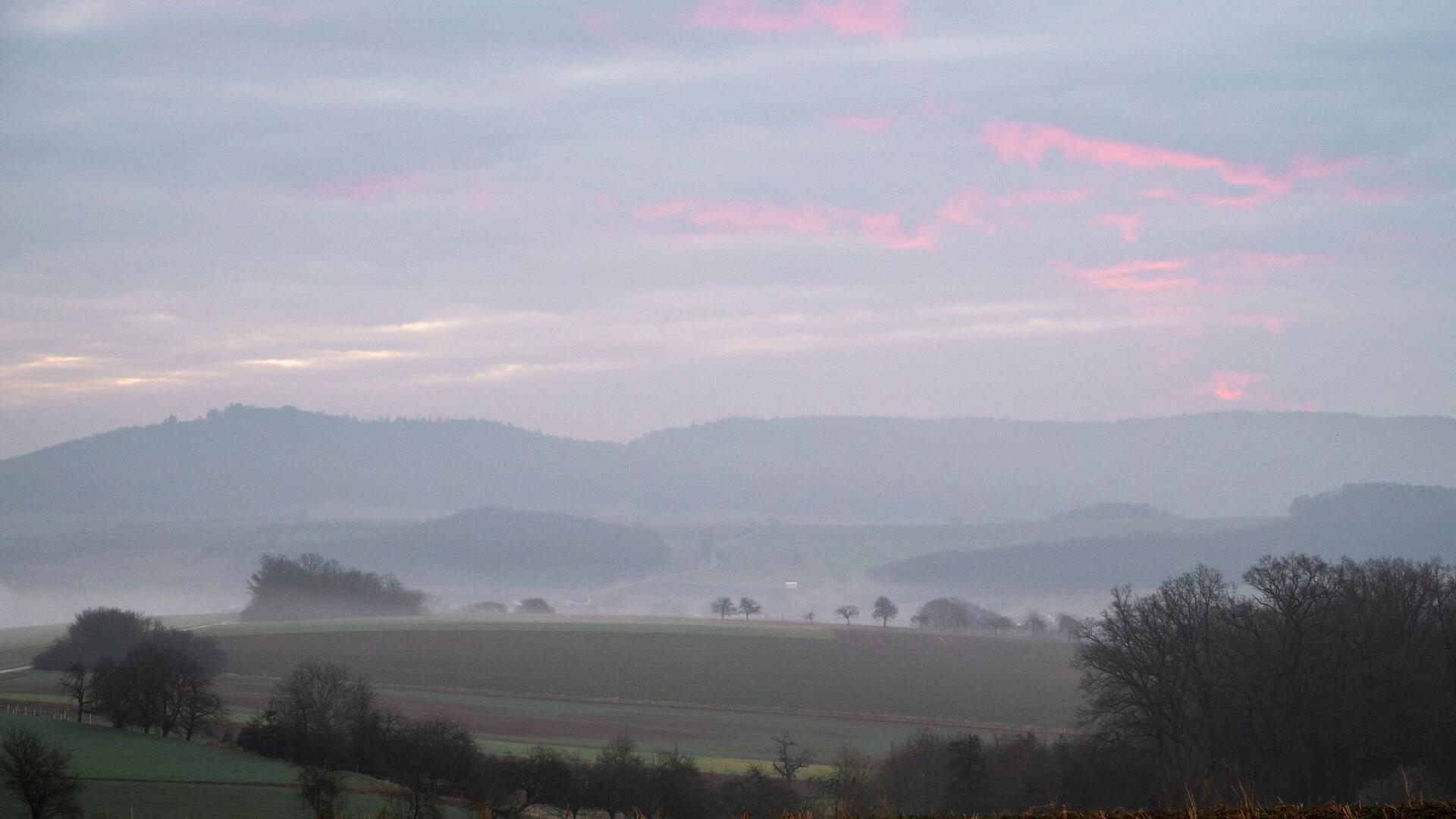 Bilder des Tages Neblige bayerische Landschaft mit Morgenrot am Himmel.