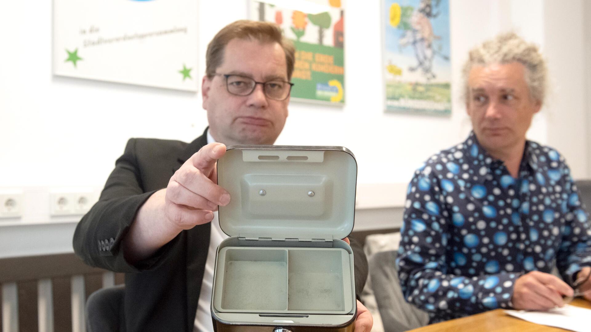 Zwei Männer, einer hält eine leeres Kassenkästchen in die Kamera
