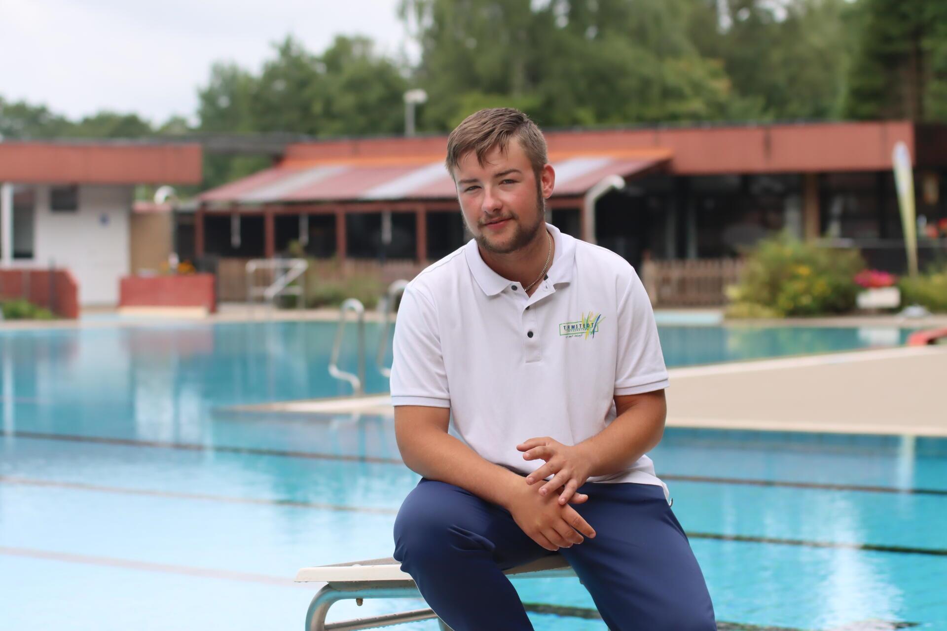Ein Mann sitzt auf einem Startblock im Freibad und blickt in die Kamera.