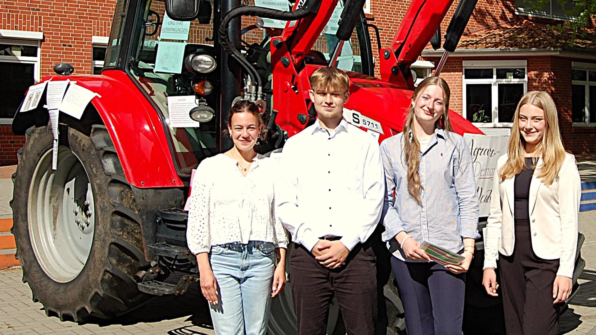 Drei Schülerinnen und ein Schüler stehen vor einem roten Traktor. 