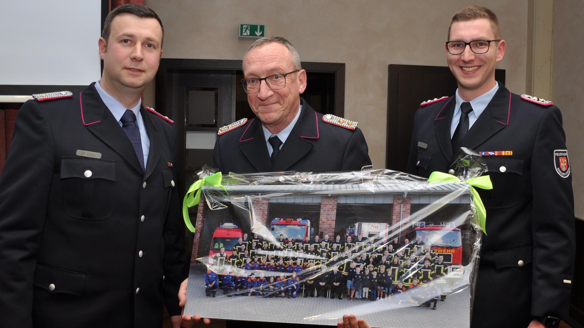 Ortsbrandmeister Hendrik Holst (links) und sein Stellvertreter Felix Haase (rechts) machen einem Mann, der die jüngere Geschichte der Bremervörder Feuerwehr wesentlich mitgeprägt hat, eine großformatige Foto-Freude: Holger Naubert, der sich zu Beginn des vergangenen Jahres aus der Führungsriege der Wehr verabschiedet hatte.