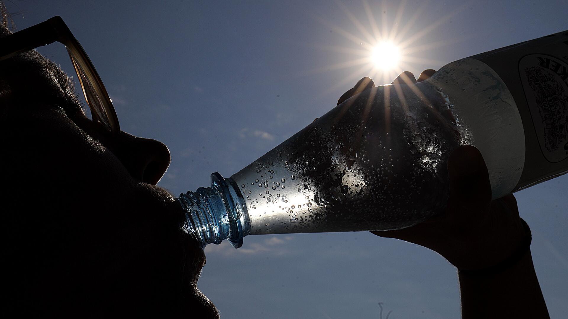 Eine Frau trinkt in der Sonne Mineralwasser.
