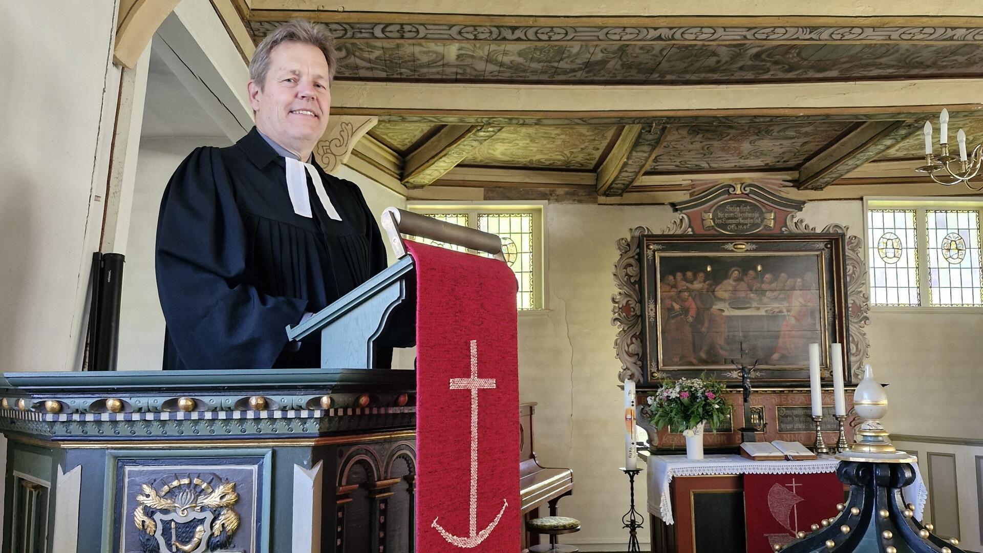 Ein Pastor im Talar steht in der Kanzel einer kleinen Kirche.