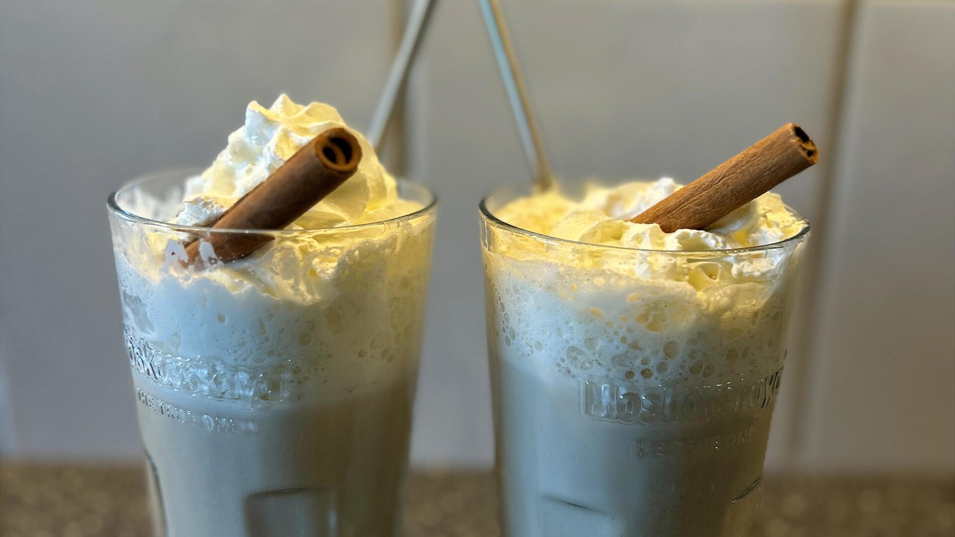 Zwei Gläser mit Latte und einer Zimtstange als Deko stehen auf einer Arbeitsfläche in einer Küche.