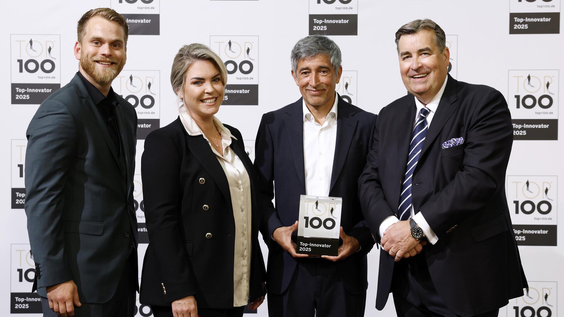 Vier Personen stehen vor einer Fotowand mit dem Logo „TOP 100 – Top-Innovator 2025“, eine Person hält die Auszeichnung in den Händen.