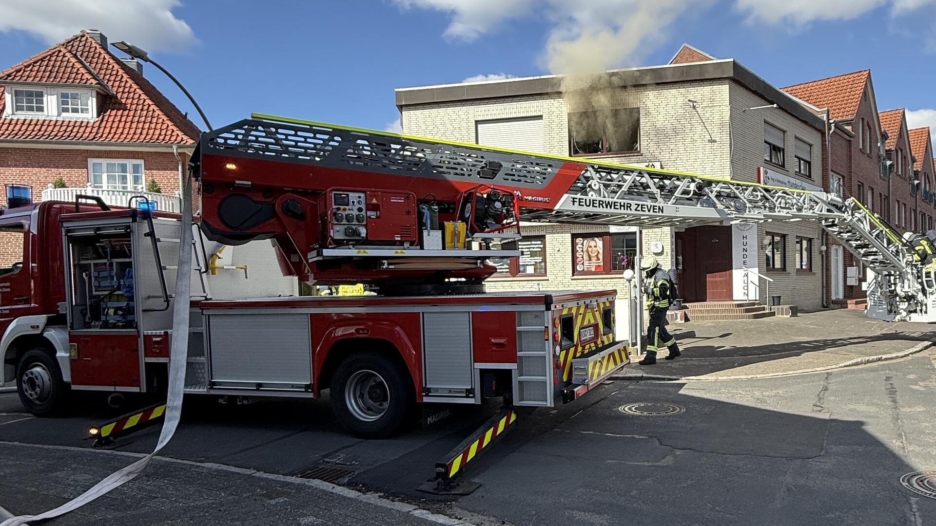 Ein Feuerwehrfahrzeug vor einem Gebäude, aus dem Rauch heruasströmt.