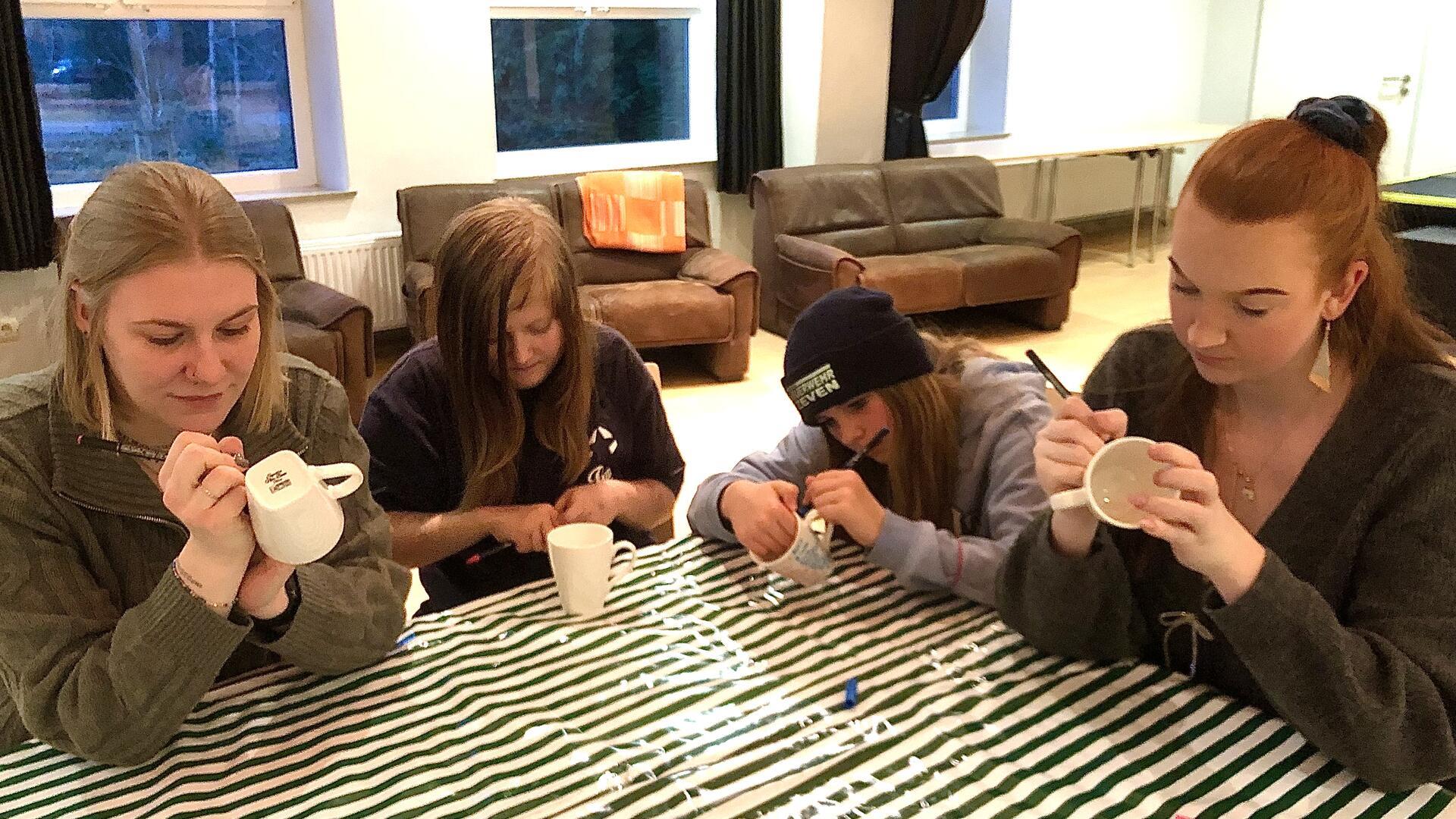 Vier Mädchen und Frauen bemalen Becher.