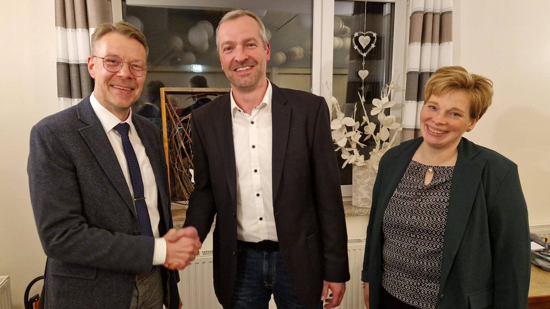 Zwei Männer schütteln sich die Hand. Eine Frau steht daneben.