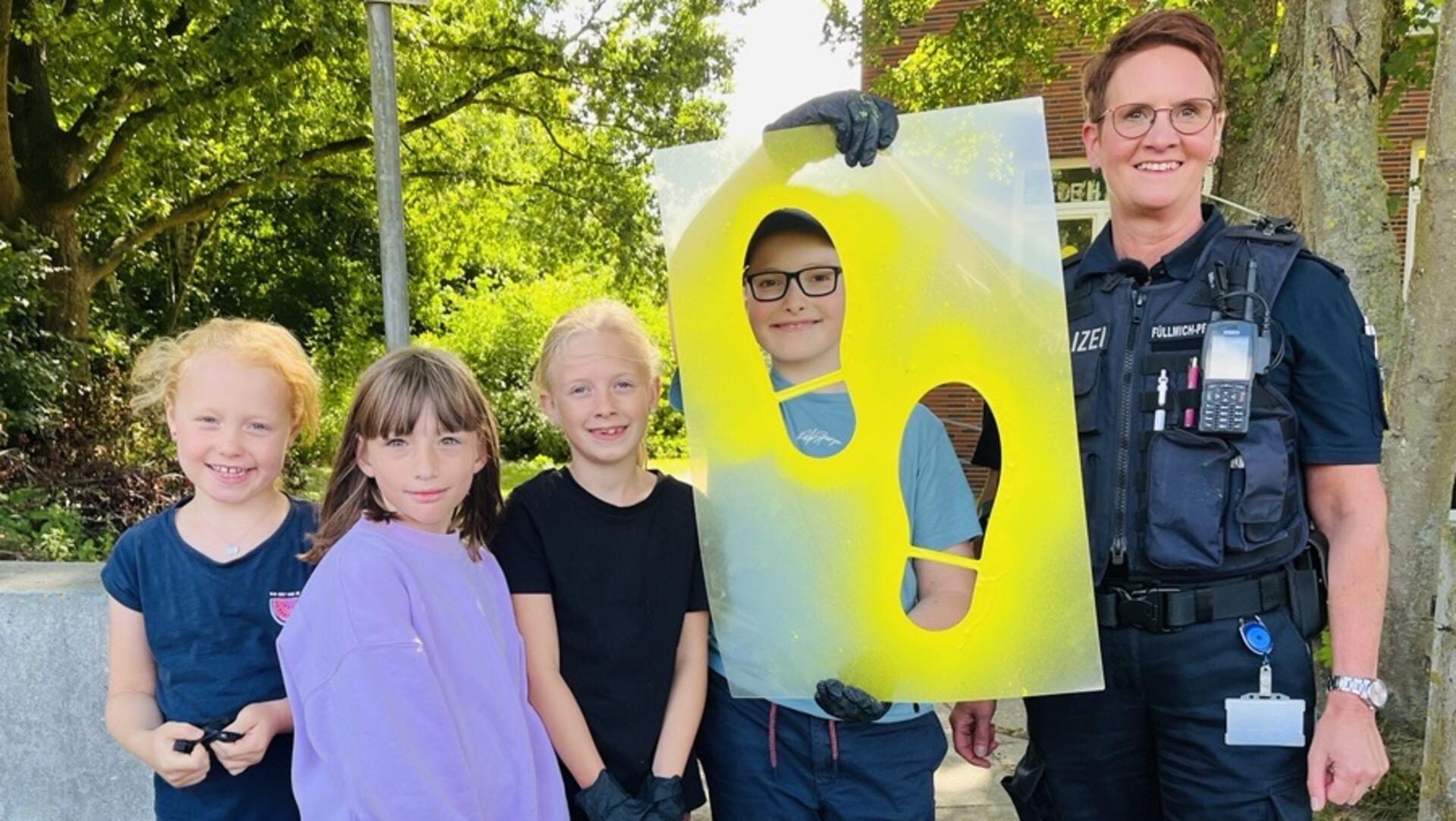 Vier Grundschulkinder mit einer Polizistin halten eine Schablone, aus der zwei Fußabdrücke ausgeschnitten sind.