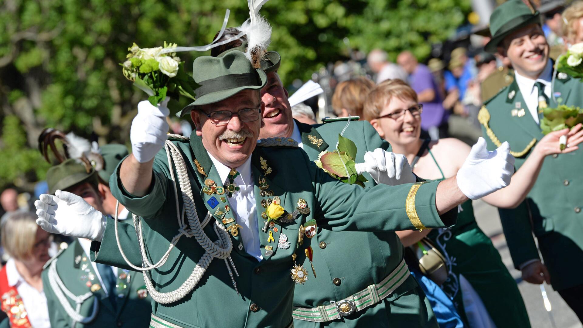 Ein Mann in einer grünen Uniform breitet lachend die Arme aus.