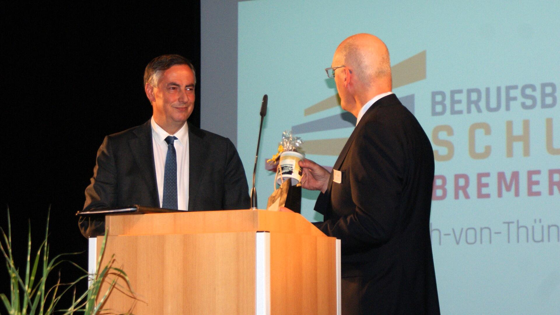 Schulleiter Lars Leminski (rechts) überreichte Festredner David McAllister einen Kaffeebecher, auf dem noch das "gelbe" Schulgebäude abgebildet ist.