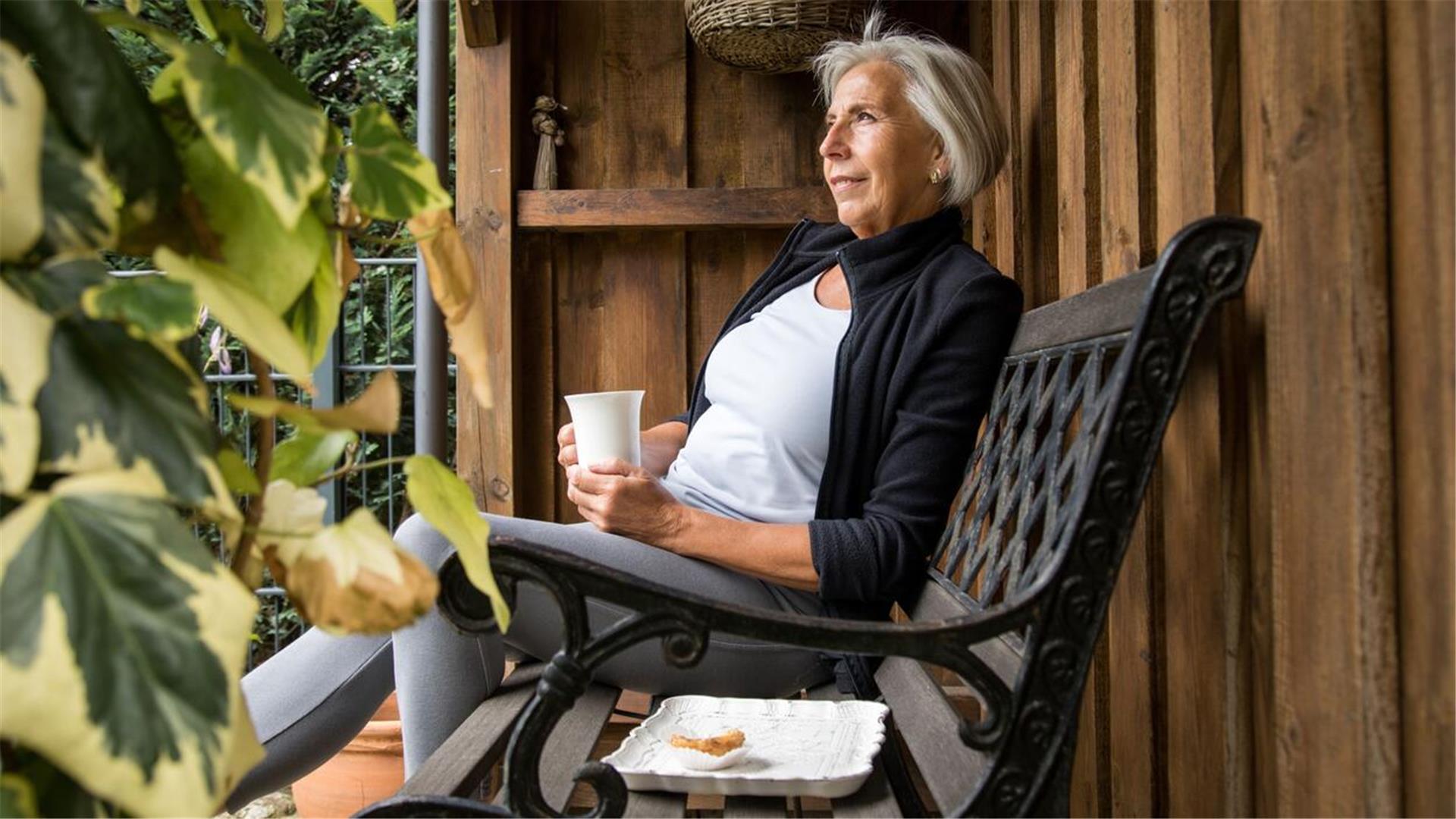Eine Frau sitzt auf einer Bank mit einem Becher in der Hand und einem Teller neben sich.