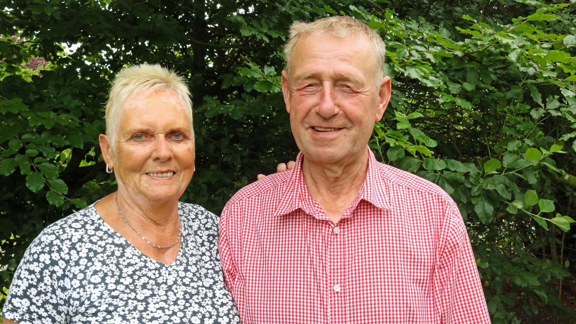 Ute und Henry Denker im Garten, rund 50 Jahre nach ihrer Hochzeit. Beide lächeln in die Kamera, im Hintergrund grünes Laub.