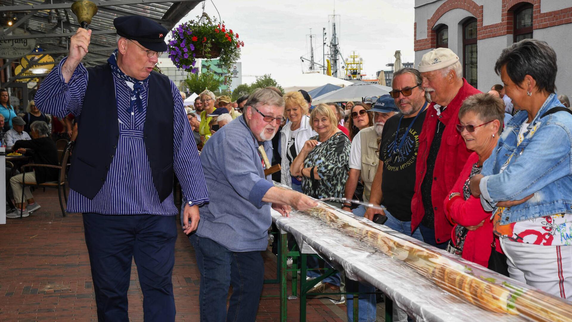 Der Matjesorden mit Sönke Allers (links) und Gerd Blancke (2. von links) verkauft ein riesiges Fischbrötchen für den guten Zweck.