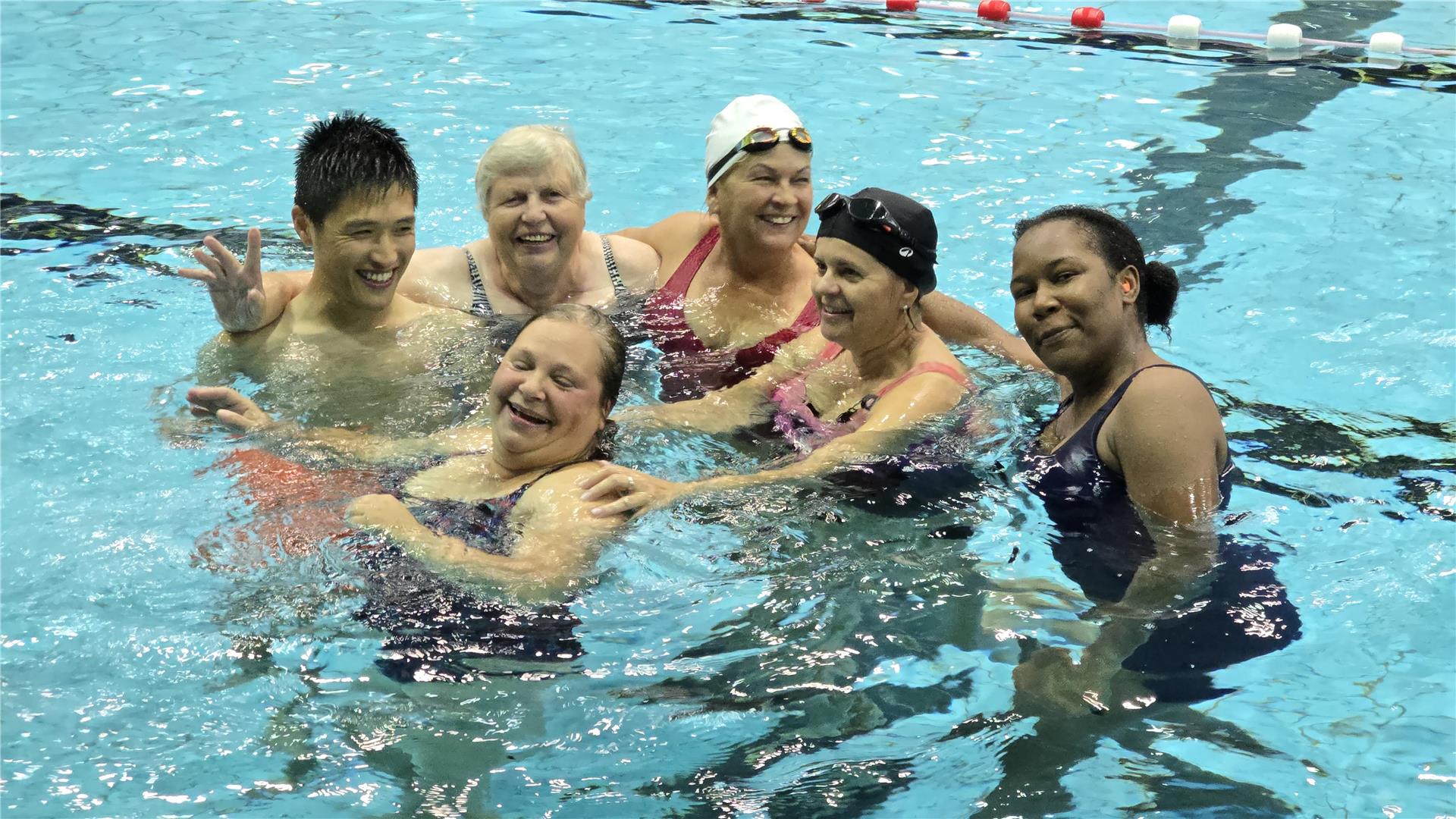 sechs gut gelaunte Personen in Badebekleidung in einem Schwimmbecken