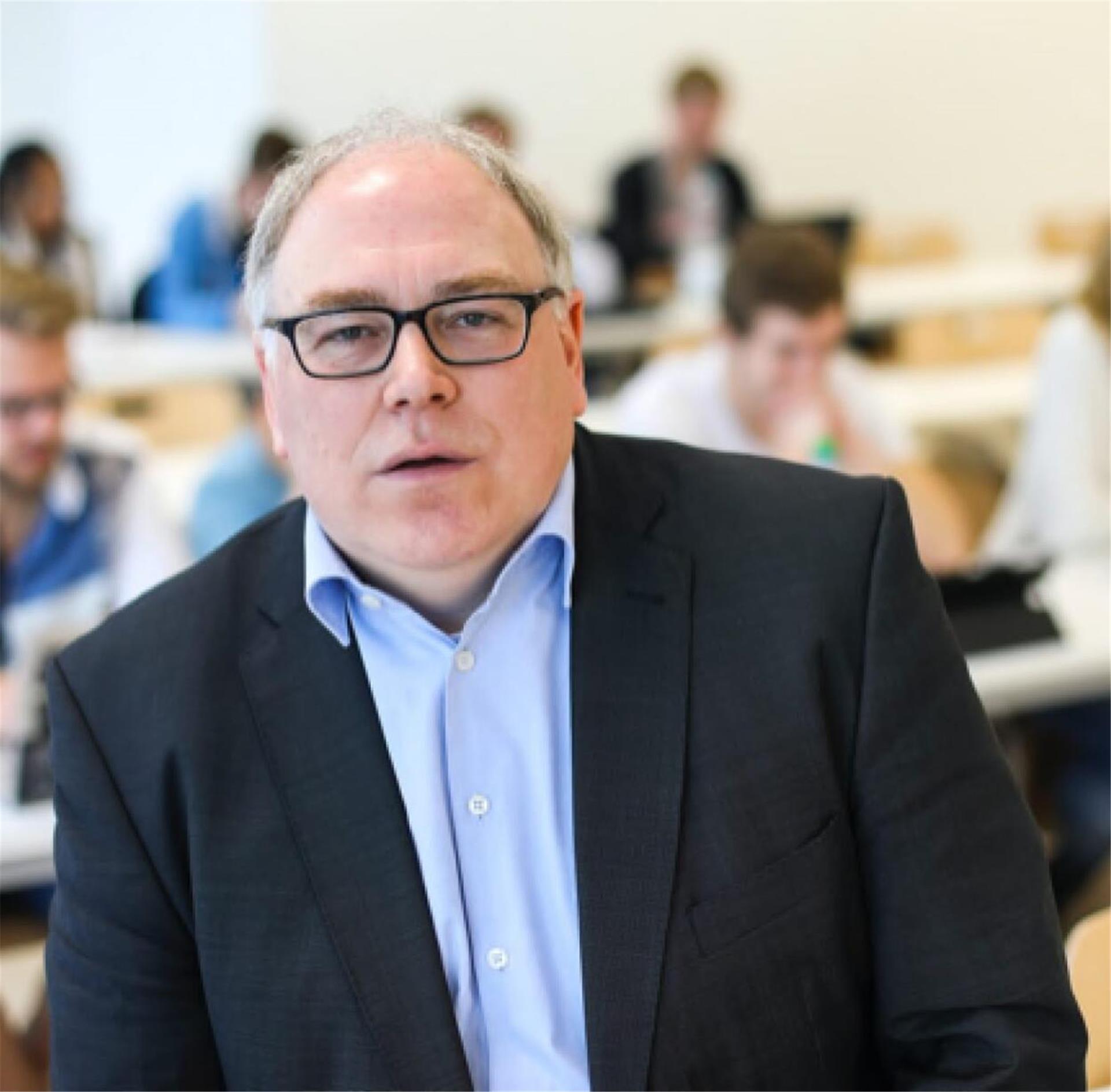 Ein Mann in einem dunklen Anzug und mit hellblauem Hemd guckt in die Kamera. Er trägt eine Brille und hat eine ohne Stirn. Es ist der Migrationsforscher Prof. Dr. Jochen Oltmer,