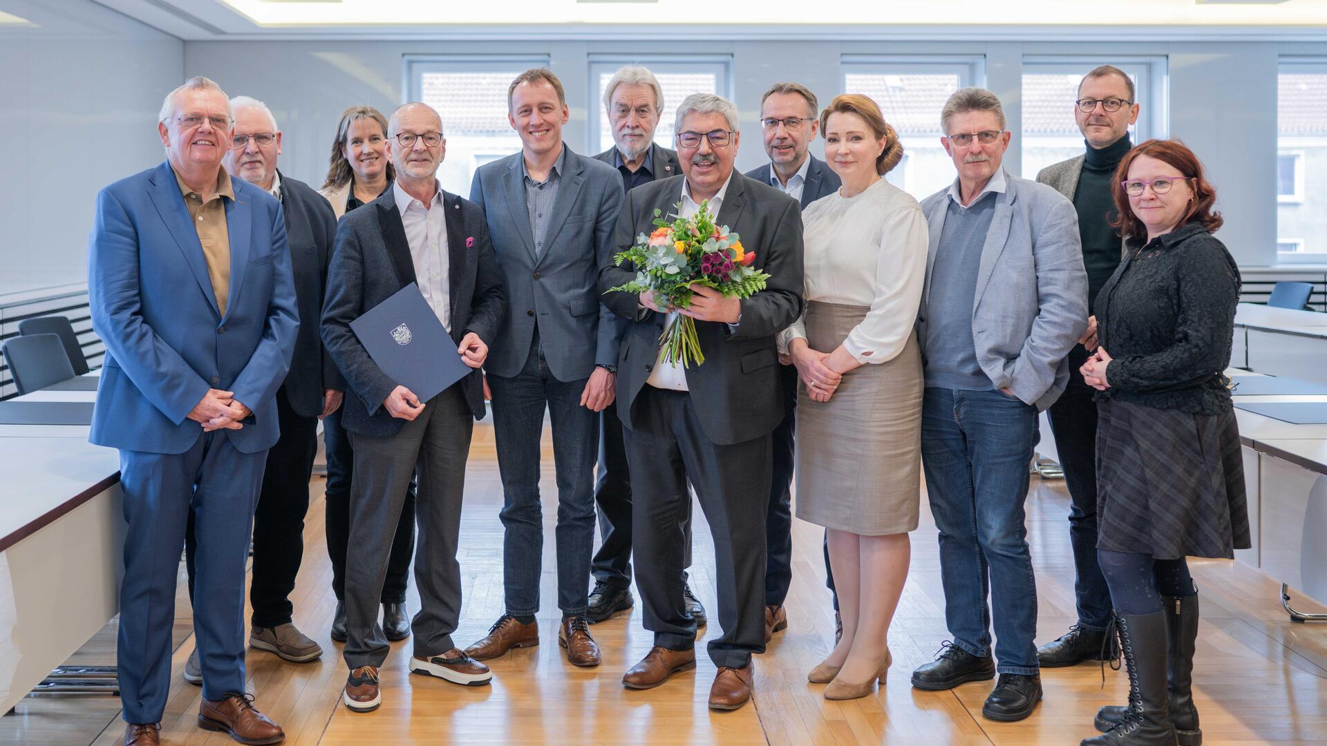 Ein Gruppenfoto mit mehreren Mitarbeitern der Stadt Bremerhaven. Der Vierte von links hält eine Urkunde in seiner Hand, ein Mann in der Mitte einen Blumenstrauß. Es geht um die Verabschiedung eines Stadtrats.