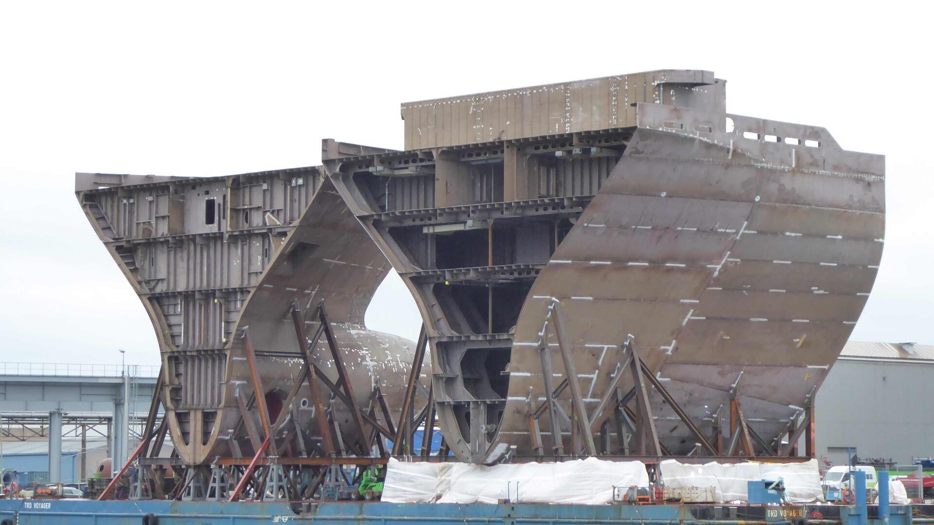 Zwei Schiffssektionen stehen auf einer Werft. 