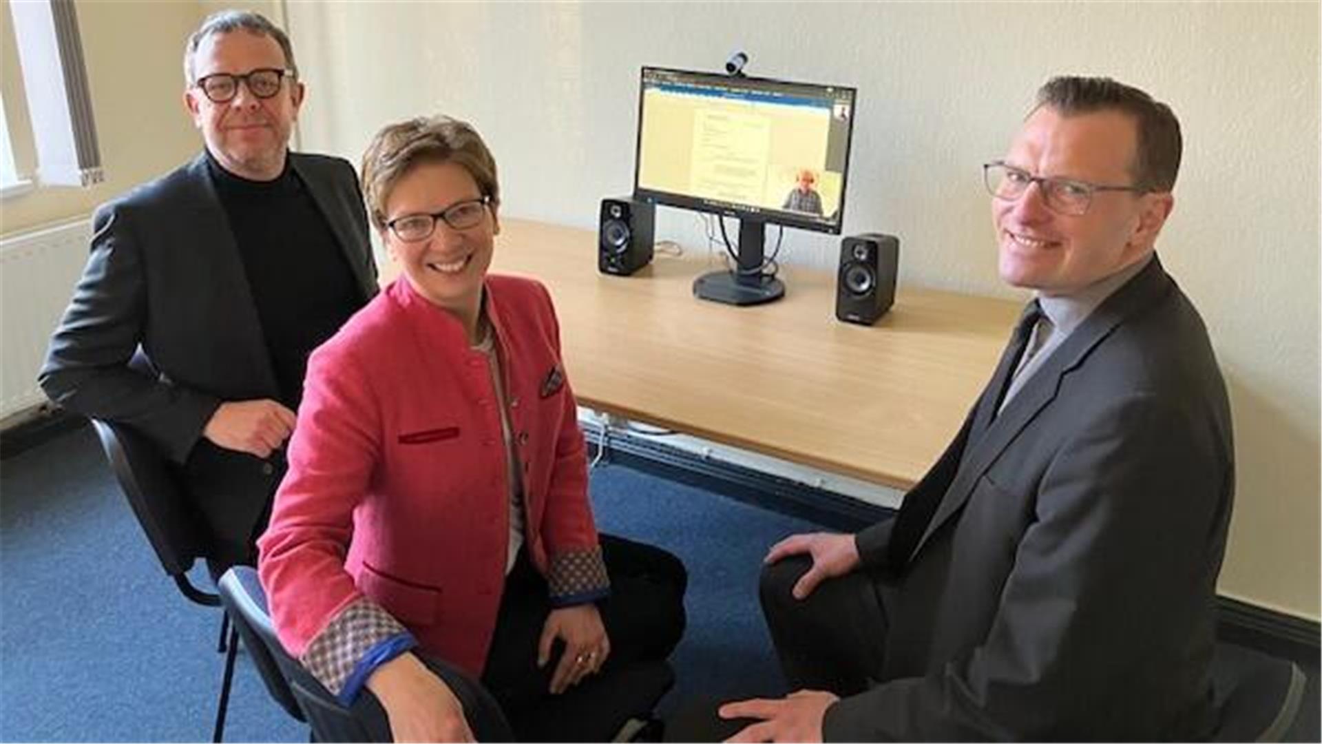 Zwei Herren (links und rechts) lächeln, eine Frau (Mitte) auch. Auf einem Schreibtisch ist ein Bildschirm zu sehen, der eingeschaltet ist. Der Start der Online-Rechtsantragstelle im Arbeitsgericht Bremen-Bremerhaven erleichtert den Bürgern den Zugang zur Justiz, indem sie Anträge und Klagen bequem von zuhause aus einreichen können.