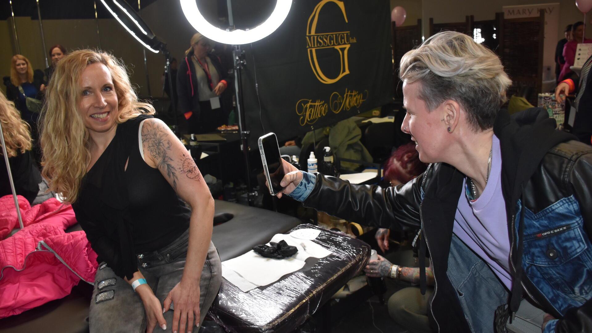 Eine Frau mit Tattoo wird von einer anderen Frau mit dem Handy fotografiert.