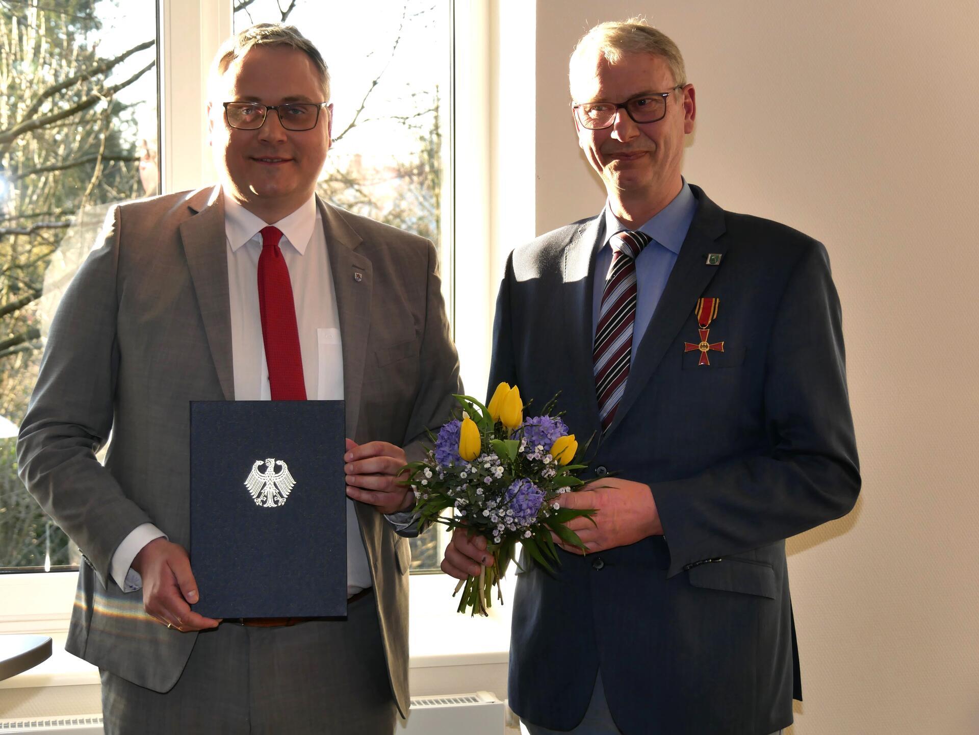 Stolz trägt Bernd Sievert (rechts) das Bundesverdienstkreuz am Revers und dankt dem Bundespräsidenten für die Auszeichnung. Landrat Marco Prietz gratuliert.
