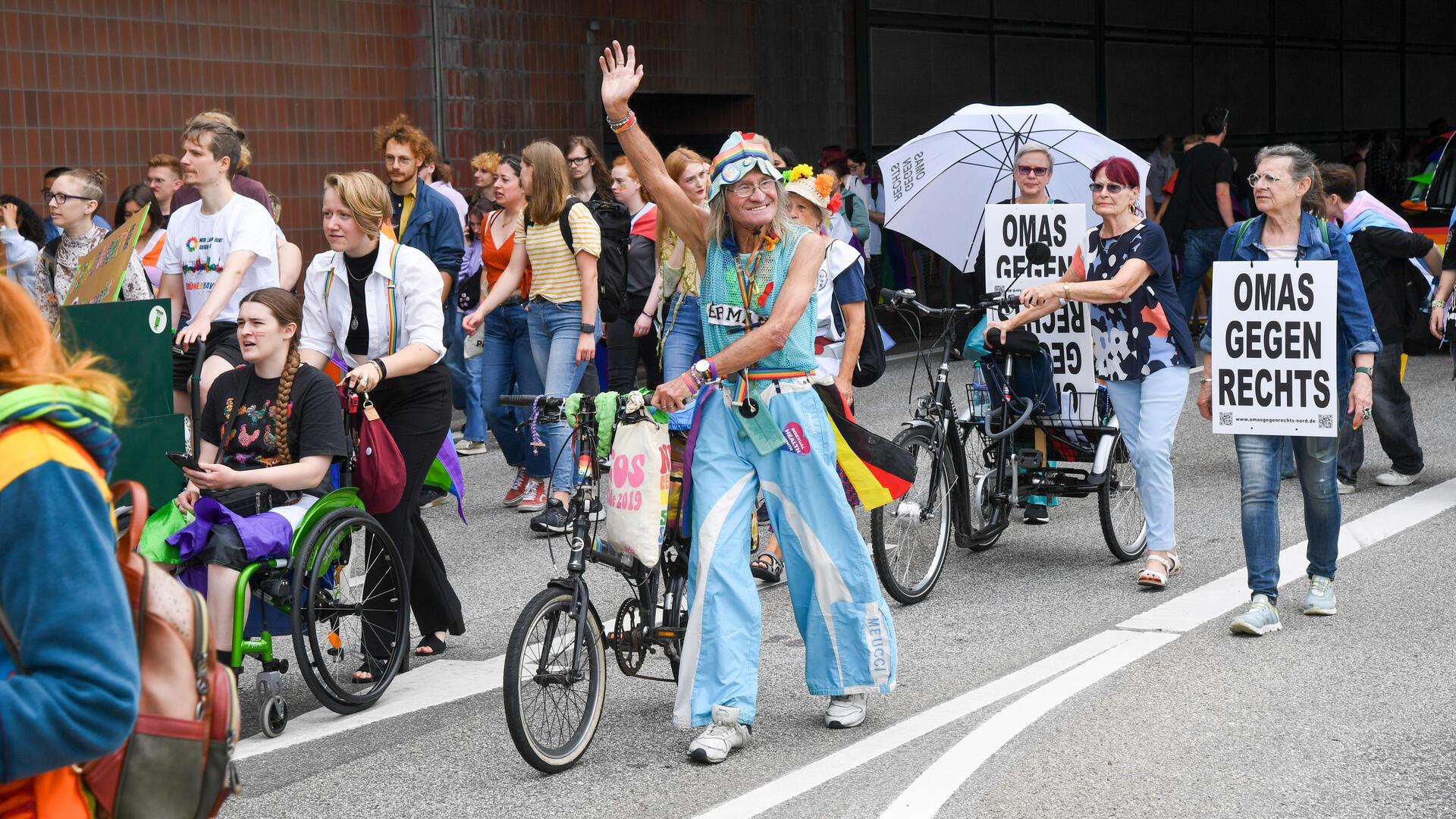 Eine Gruppe von Menschen, die am Christopher-Street-Day teilgenommen haben. In der Mitte ist eine ältere Frau mit Deutschlandfahne und einem Fahrrad, dahinter eine Frau mit einem Plakat und der Botschaft: Omas gegen rechts.   