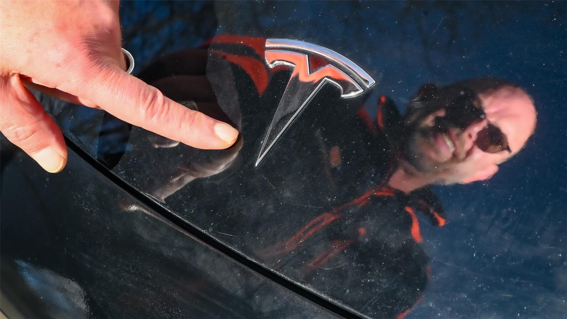 Ein Mann zeigt auf das Tesla-Symbol auf einem Wagen. 
