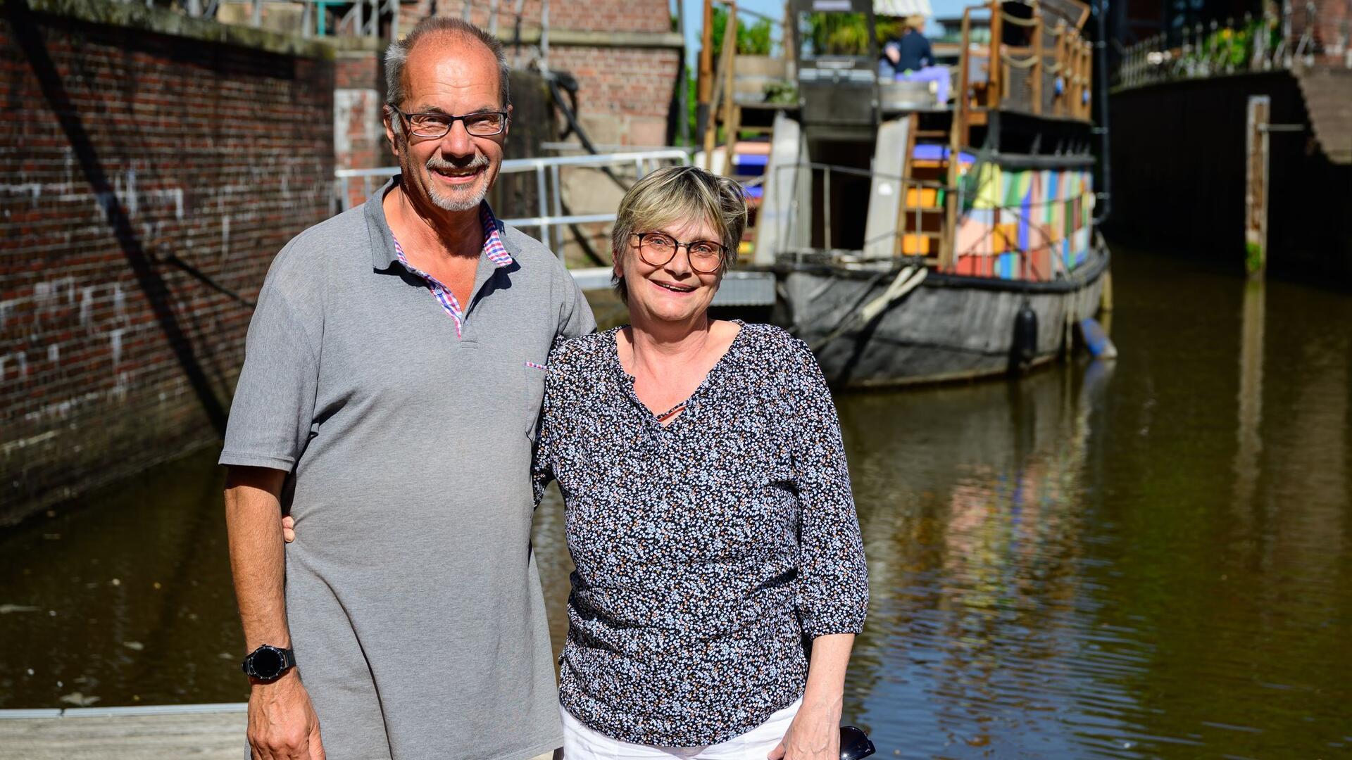 Ein älteres Paar steht an einem Hafenbecken vor einem Schiff. 