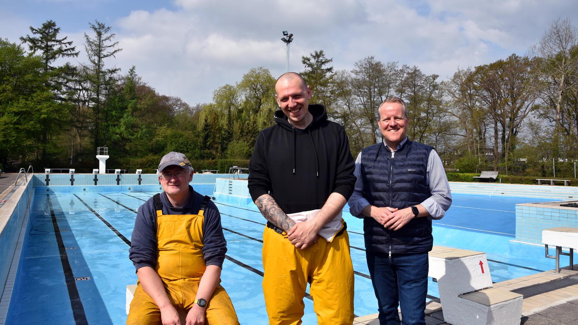 Drei Männer vor einem Schwimmbecken.