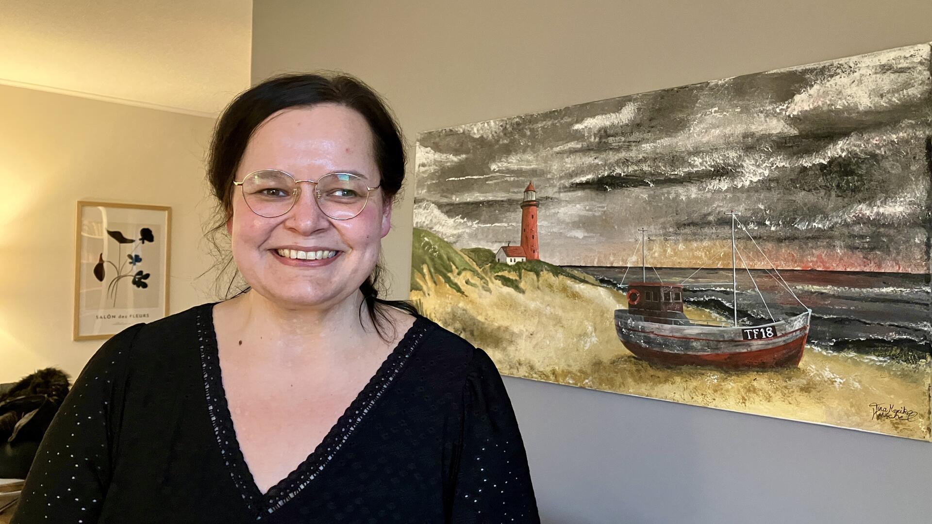 Eine Frau steht lächelnd vor einem maritimen Wandbild.