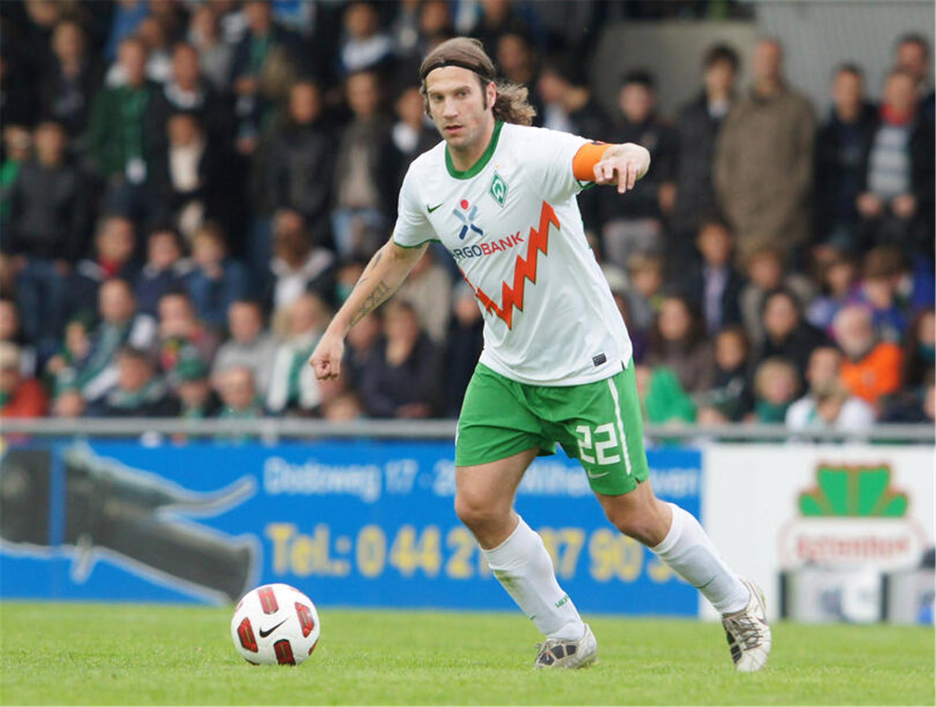 Fußballspieler mit langen Haaren und grün-weißem Trikot im Spiel in einem voll besetzten Stadion