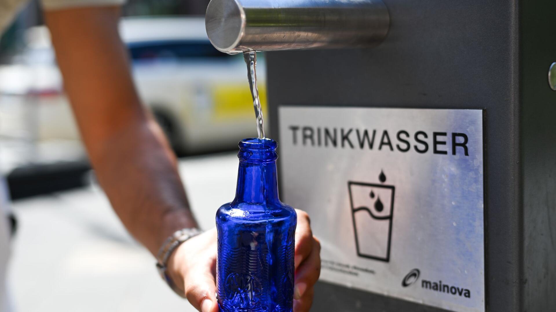 Aus einem Trinkwasserbrunnen wird Wasser in einen Behälter abgefüllt.