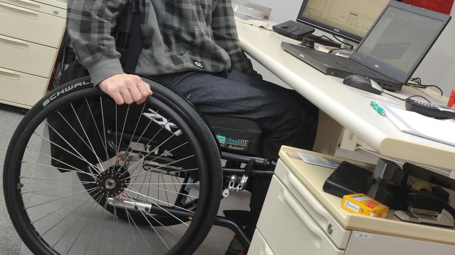 Mann sitzt mit Rollstuhl am Schreibtisch. 