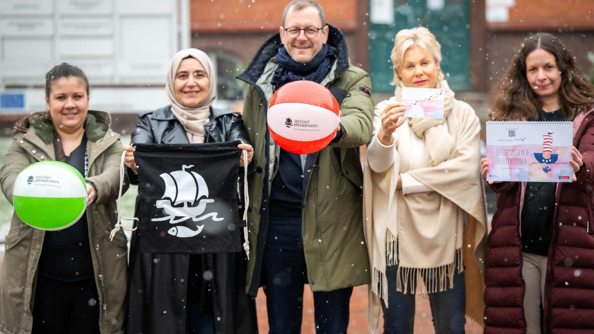 Vier Frauen und ein Mann stehen nebeneinander. In der Hand halten sie verschiedene Geschenke (Ball, Turnbeutel, Broschüren).