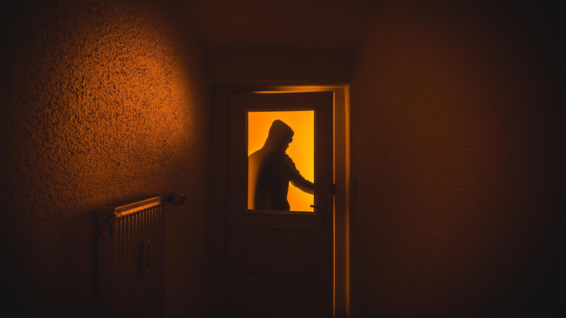 Die Silhouette eines Mannes mit Kapuze ist hinter einer Scheibe zu sehen. 