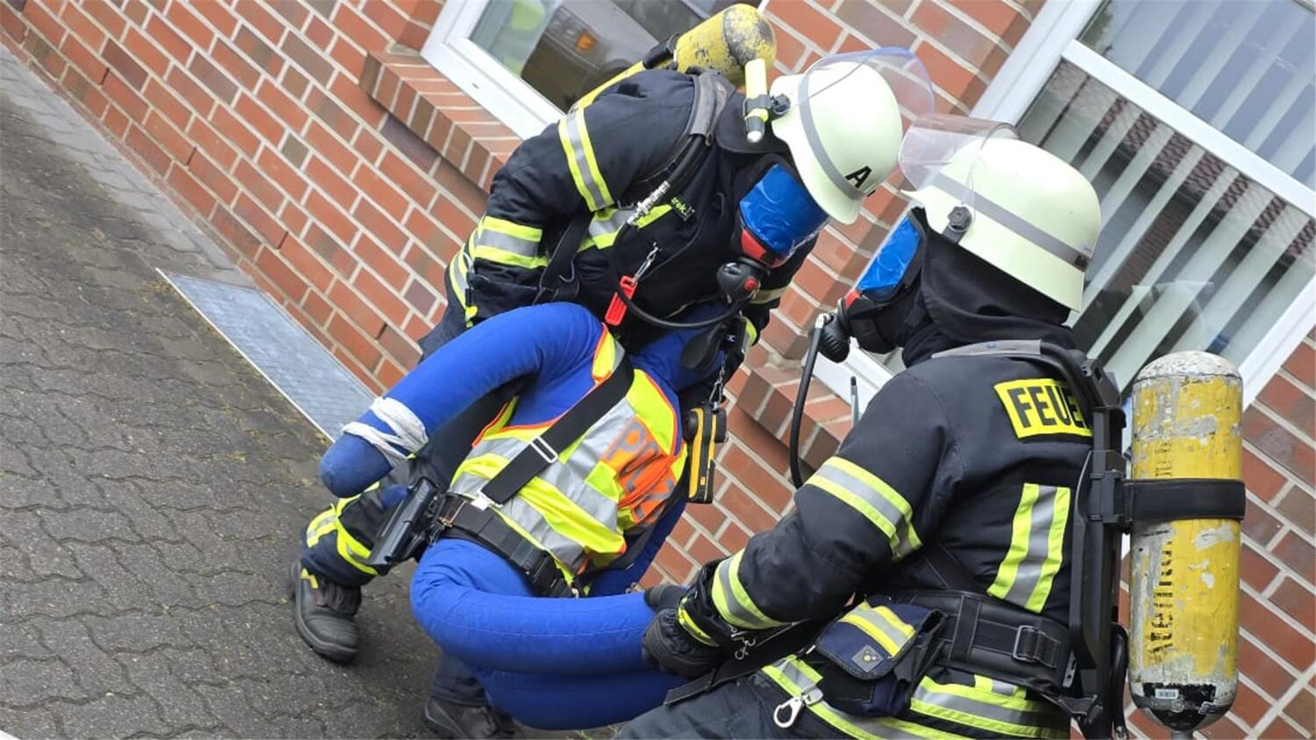 Unter Atemschutz bergen die Feuerwehrleute eine bewusstlose Person aus dem völlig verrauchten Gebäude.