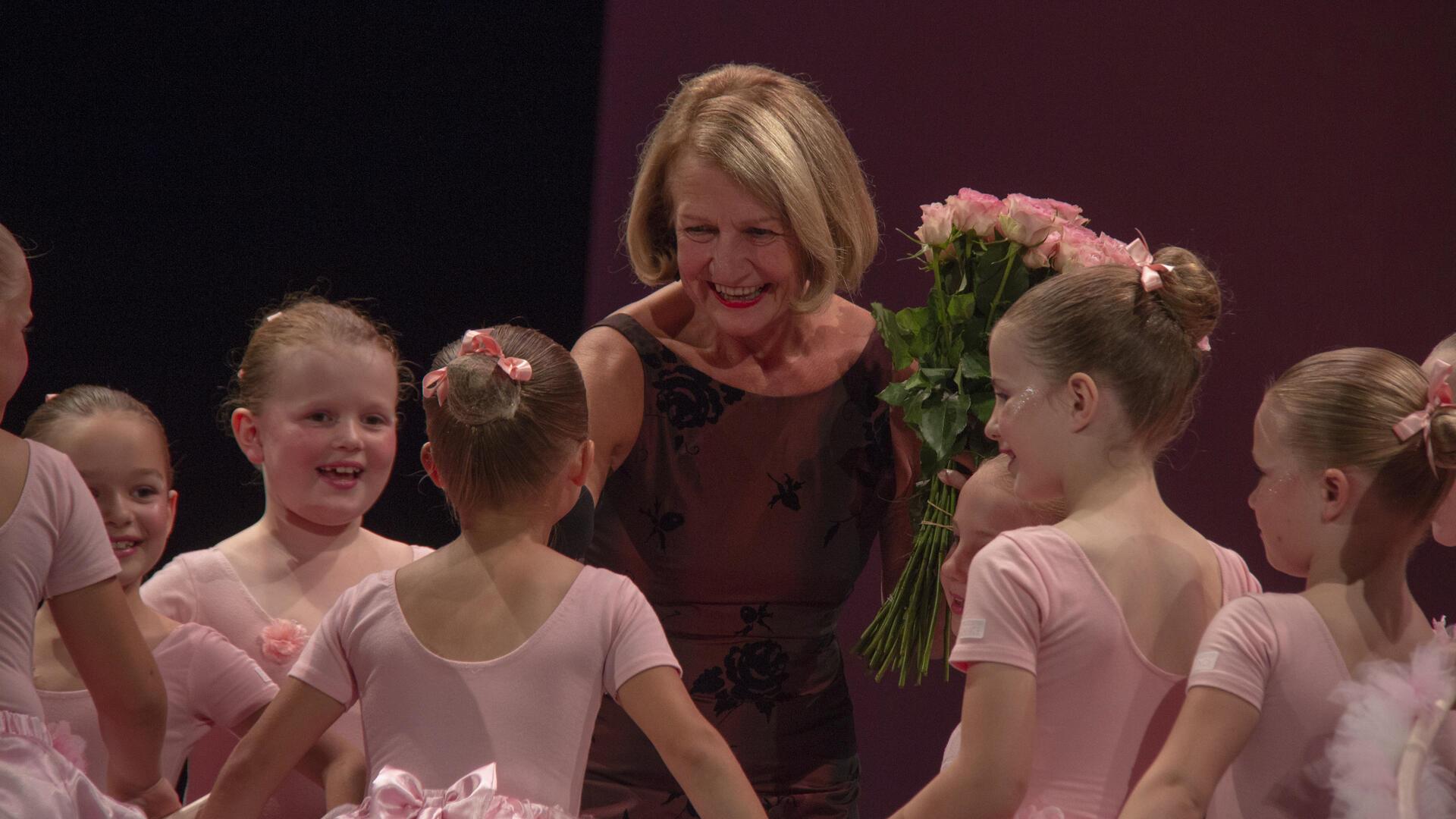 Eine Frau mit Rosen in der Hand inmitten von kleinen Ballettschülerinnen