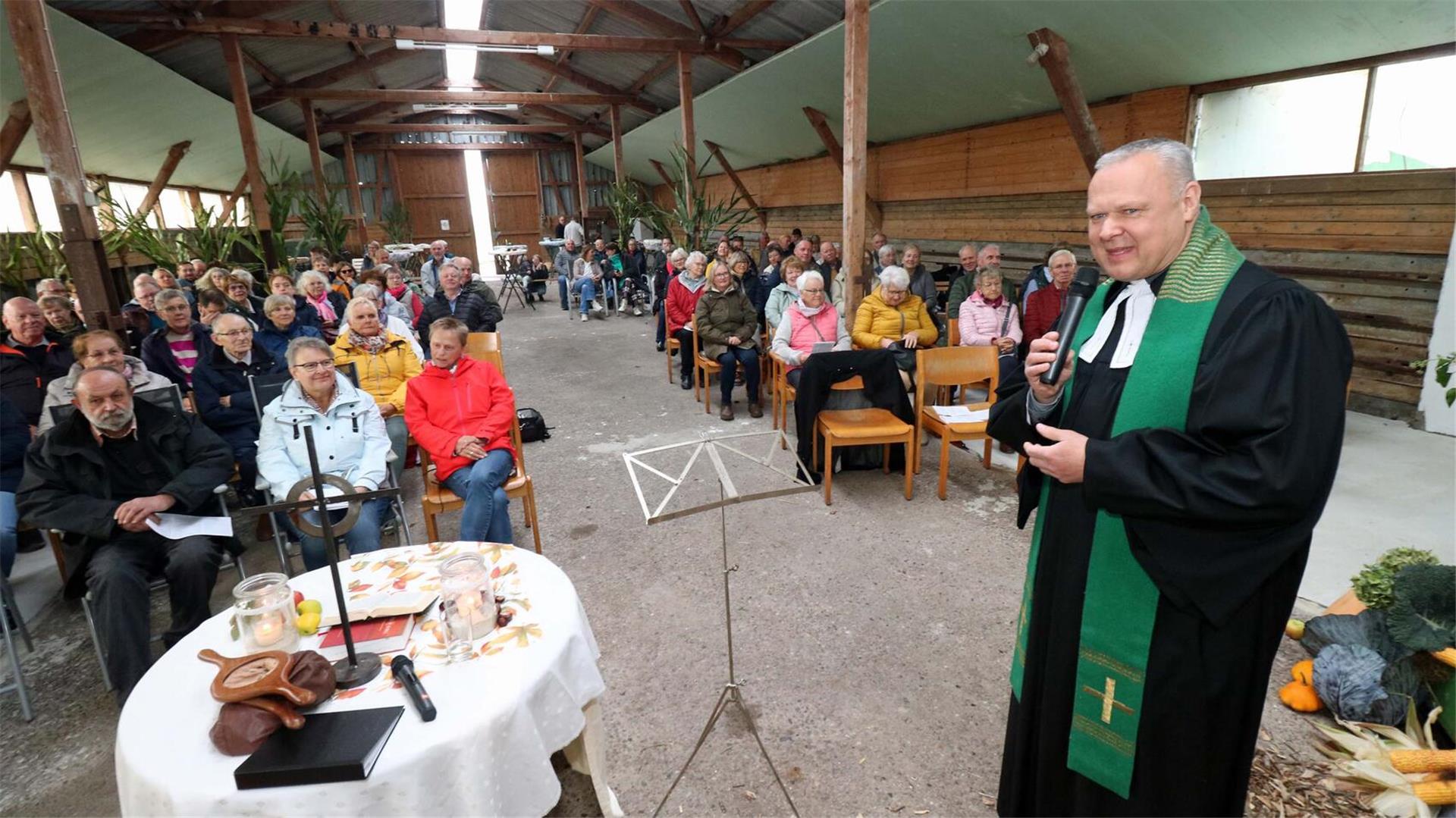 Pastor Clemens Bloedhorn spricht beim Erntedankgottesdienst in einer festlich geschmückten Bauernhofhalle in Sandstedt vor rund 150 Besucherinnen und Besuchern.