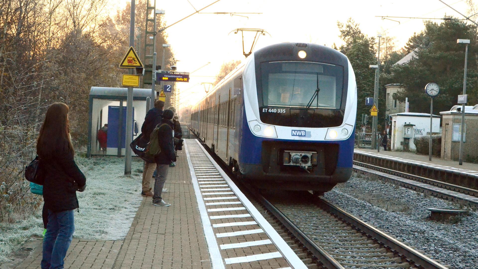 Ein Zug an einer kleineren Haltestelle. Auf dem Bahnsteig warten Menschen auf den Zug.  